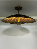 A modern semi-flush mount ceiling light fixture with a bronze metal shade in a scalloped, petal-like design, casting a warm golden glow downward against a plain white wall.