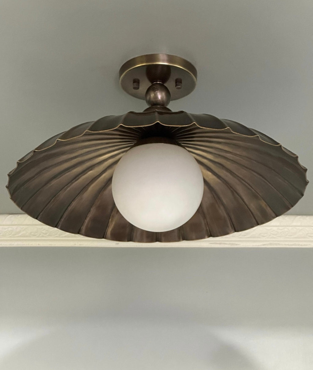 A semi flush mount light fixture with antique brass finish and milk glass globe.