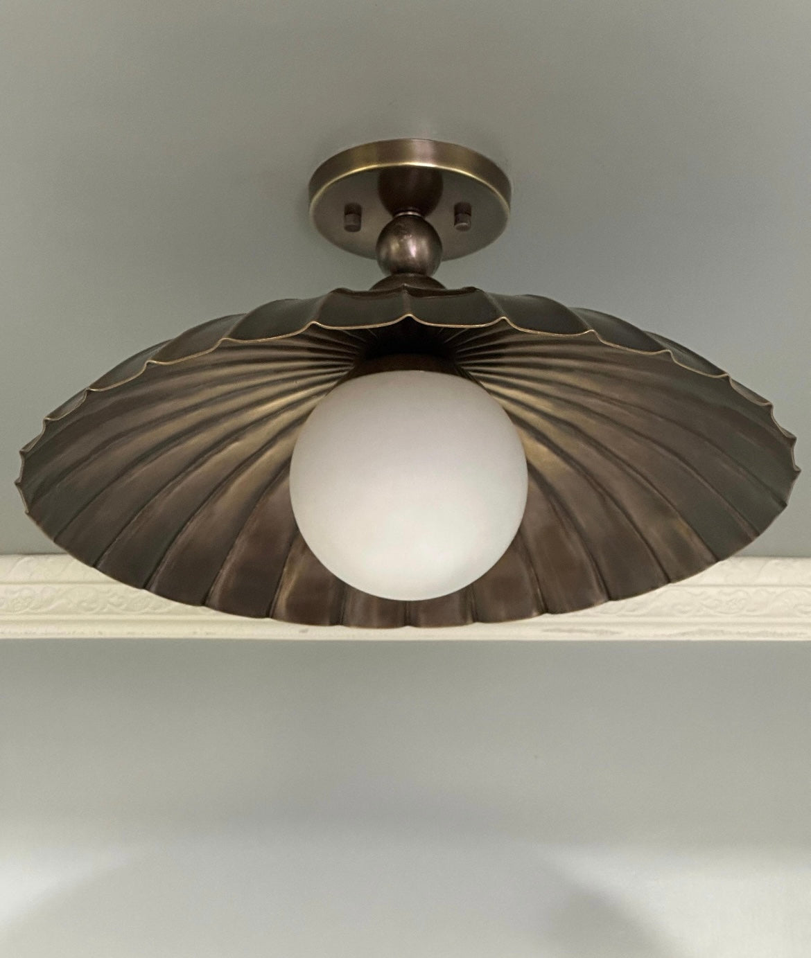 A semi flush mount light fixture with antique brass finish and milk glass globe.
