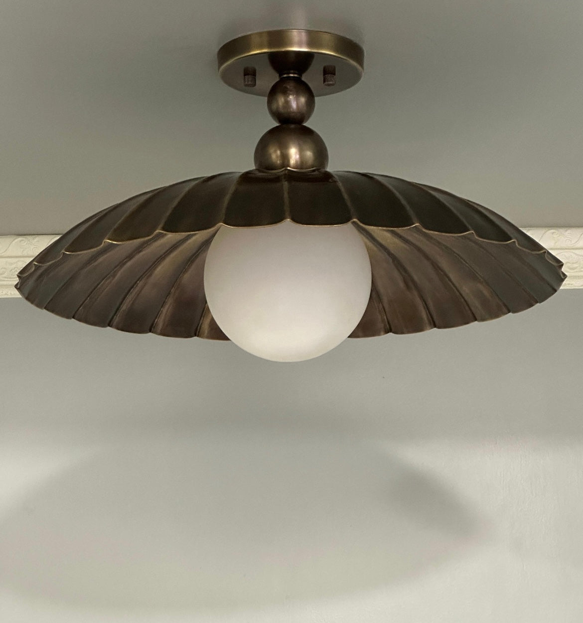 An industrial-style ceiling light fixture with a bronze-toned metal fluted shade and a frosted white glass globe bulb, shown installed against a neutral gray ceiling.