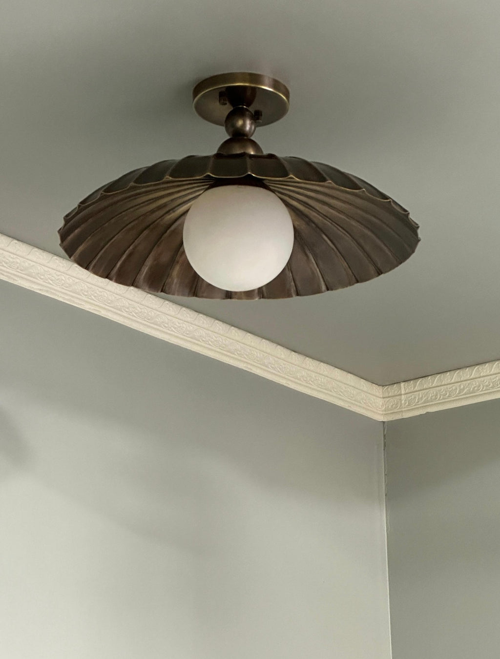 A ceiling-mounted light fixture with a dark bronze or gunmetal fluted shade and a white frosted globe bulb, shown installed on a ceiling corner.