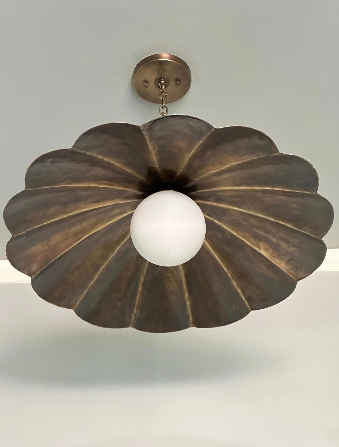 A vintage-style pendant light with a large, scalloped bronze metal shade and a central white glass globe, suspended from a matching bronze ceiling canopy.