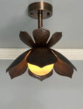A ceiling-mounted pendant light fixture with a dark bronze metal frame shaped like a lotus flower, featuring carved leaf-like petals and a glowing warm yellow globe bulb.