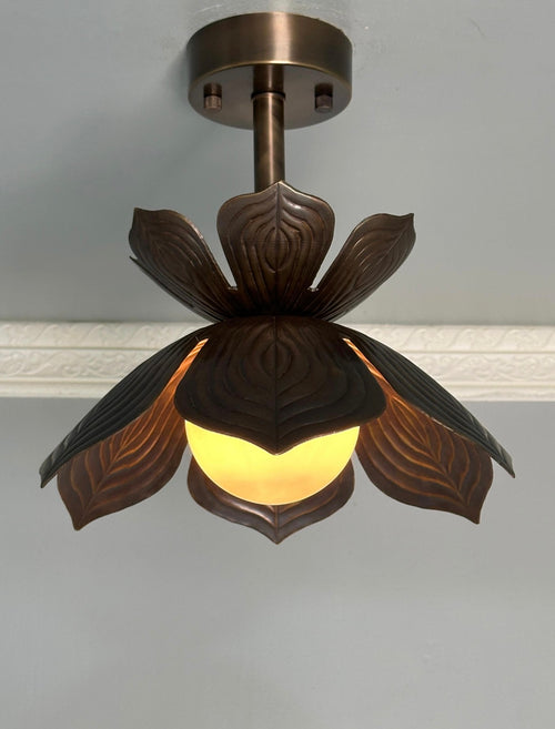 A ceiling-mounted pendant light fixture with a dark bronze metal frame shaped like a lotus flower, featuring carved leaf-like petals and a glowing warm yellow globe bulb.
