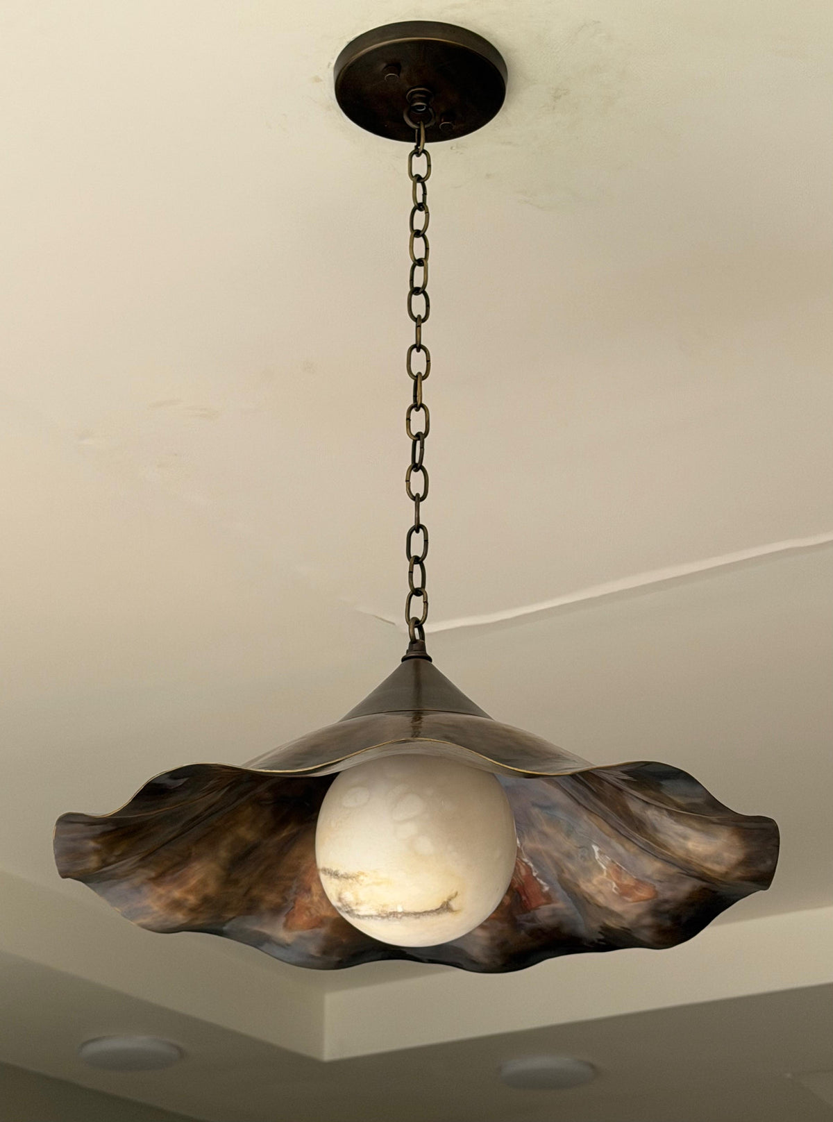 Close up of ruffled brass pendant light with white glass globe